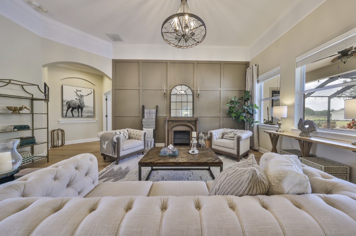 Formal living room with beaded chandelier, board-and-batten accent wall, tufted Chesterfield sofas, and arched mirror over fireplace — Lithia, FL